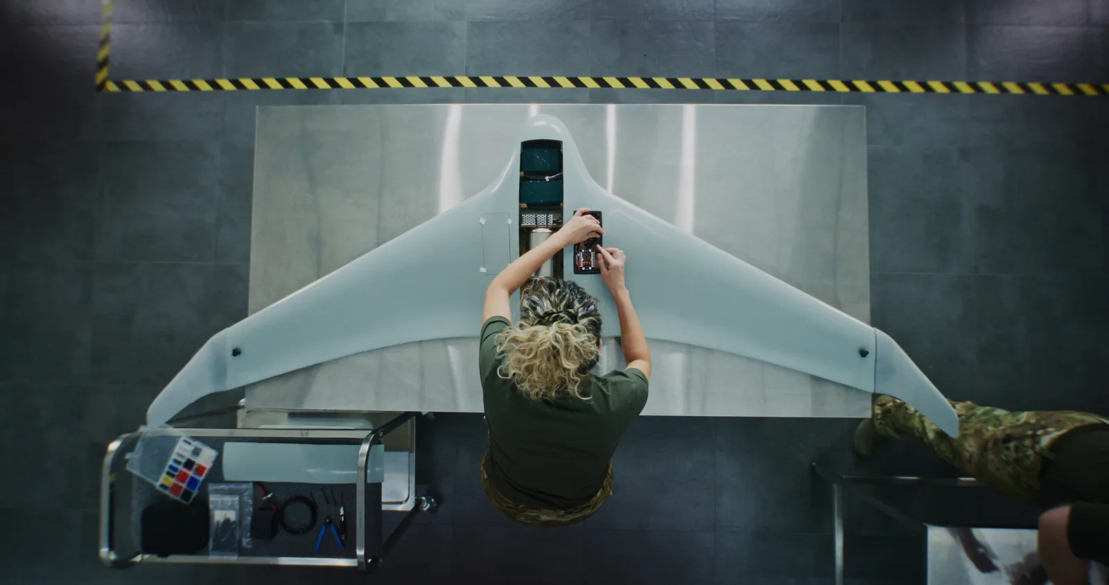 Overhead view of a technician assembling a UAV airframe at a forward manufacturing station